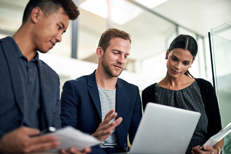 Three people standing, looking at laptop
