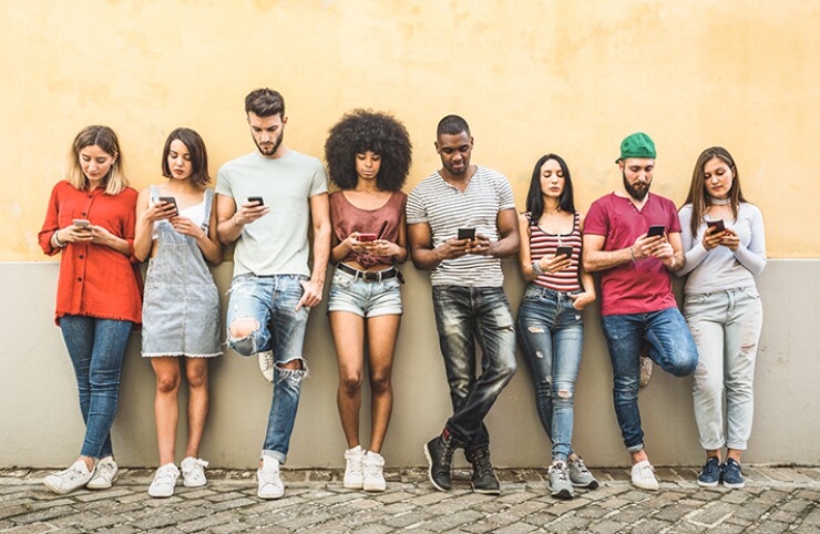 A group of young people against a wall, looking at their smart phones.