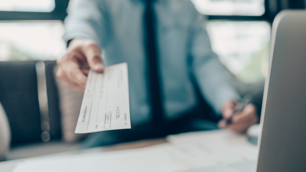 A man wearing a dress shirt and tie hands the camera operator a check