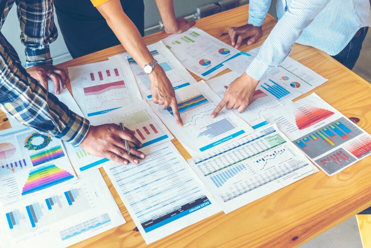 Employees looking and pointing at data, lots of data printed on table