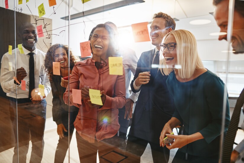 Colleagues are laughing as they place post-it notes on a glass wall.