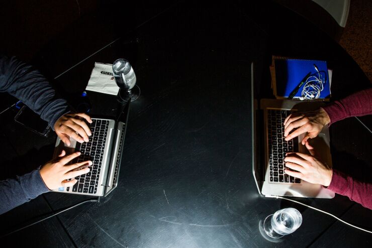 Two people work on laptops across from one another, as pictured from above.