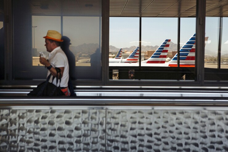A traveler passes in front of American Airlines planes reflected in a window at Phoenix Sky Harbor International Airport (PHX) in Phoenix, Arizona, U.S., on Thursday, July 5, 2018.