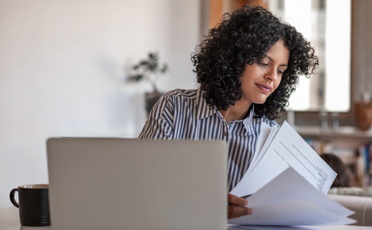 Woman looking over paperwork, sitting in front of laptop computer