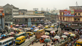 An overhead view of people, cars and market stalls on a street.