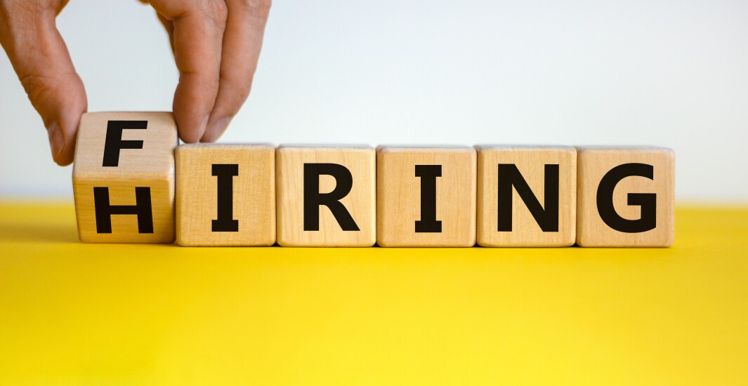 Hiring or firing symbol. Businessman hand turns a wooden cube and changes the word 'firing' to 'hiring'. Beautiful yellow table, white background, copy space. Business and hiring or firing concept.