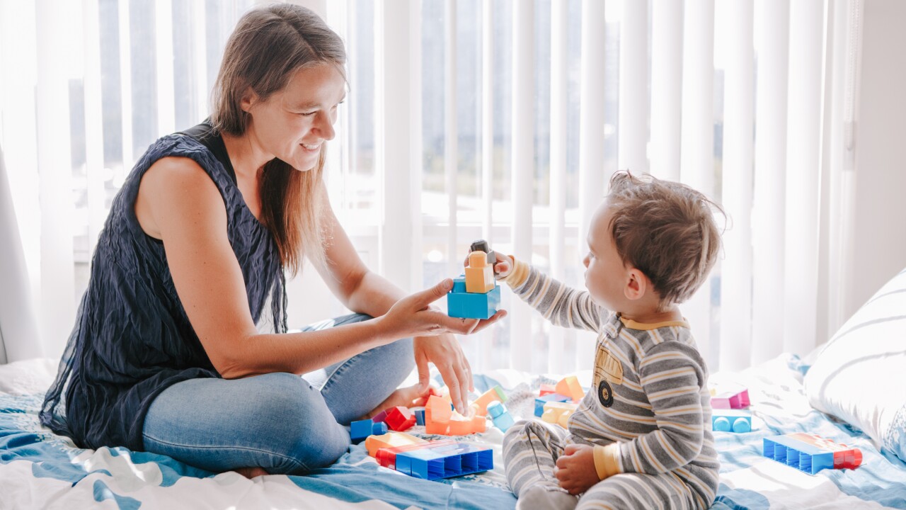 Mother playing blocks with child on bed