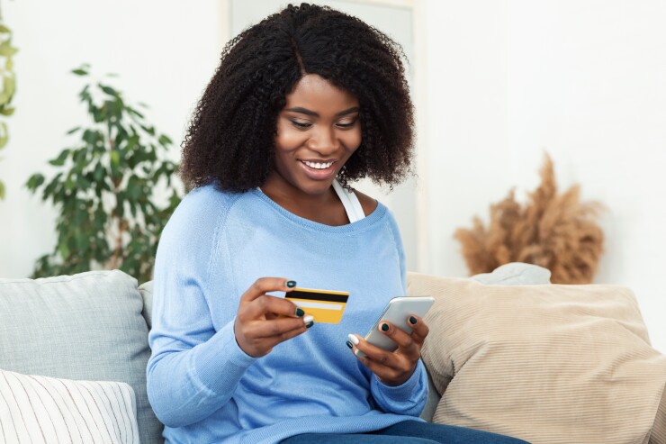Woman holding credit card and cell phone smiling on couch