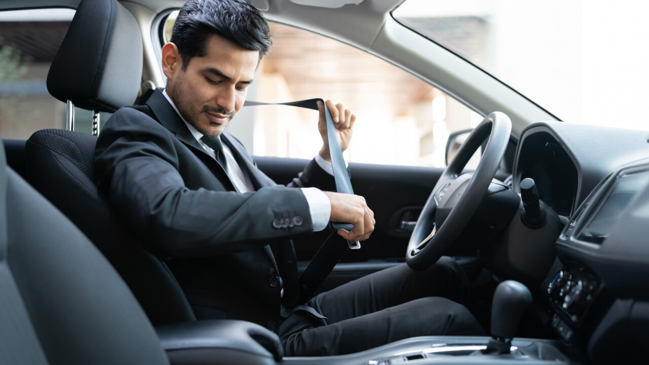 Man in suit sitting in car buckling seatbelt