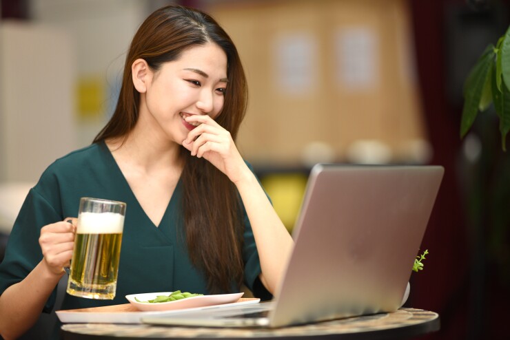 Woman holding a beer while laughing in front of her laptop
