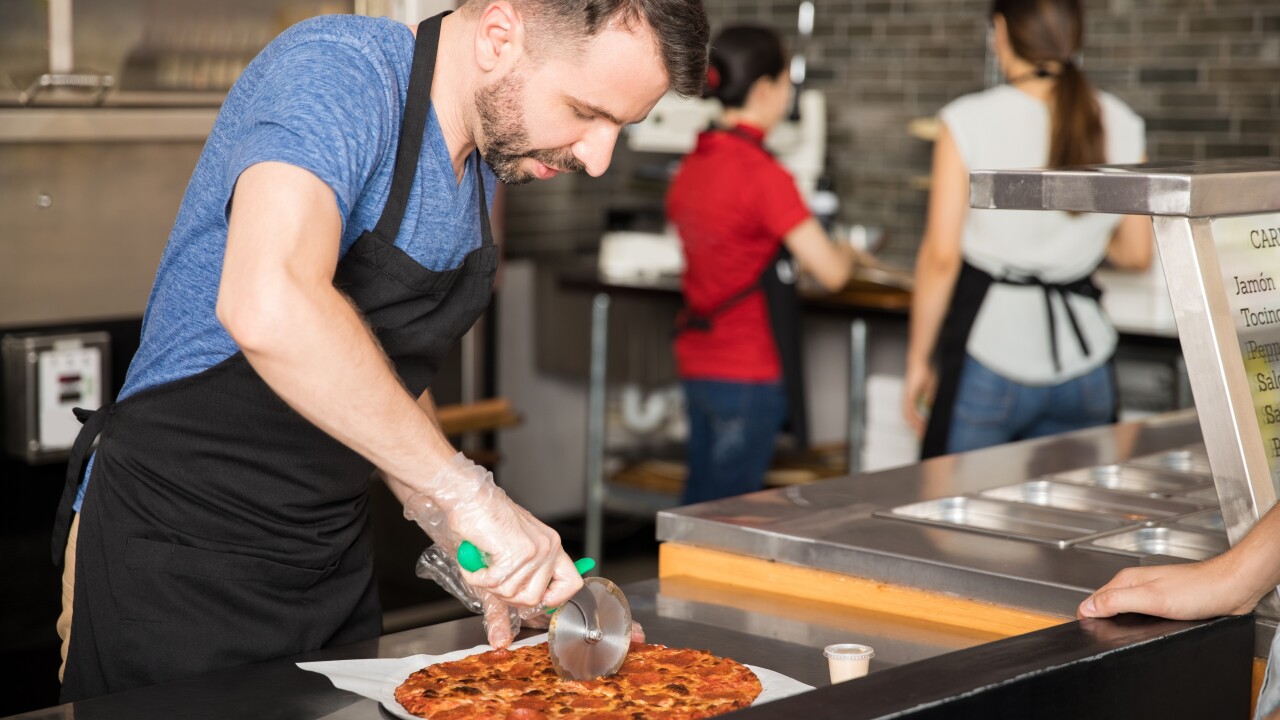 Employee cutting pizza in restaurant