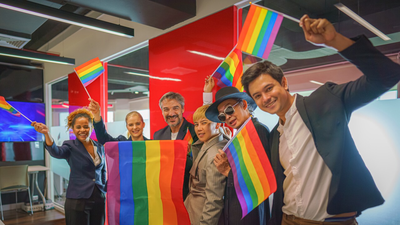 Colleagues wave rainbow flags in the office together.