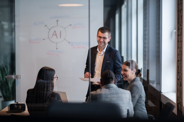 A man talks to three co-workers in a board room.