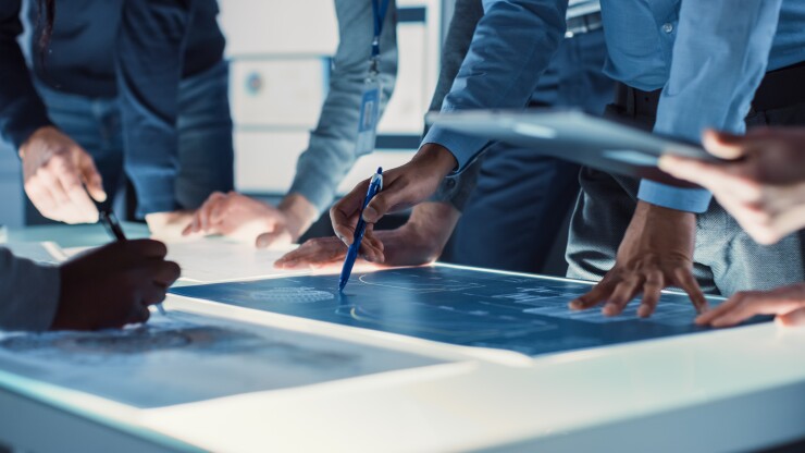 People gathered around an illuminated conference table looking at papers.