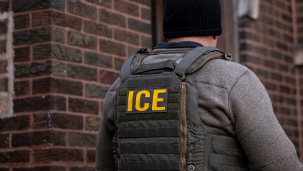 A U.S. Immigration and Customs Enforcement (ICE) agent outside an apartment building during a multi-agency targeted enforcement operation in Chicago.