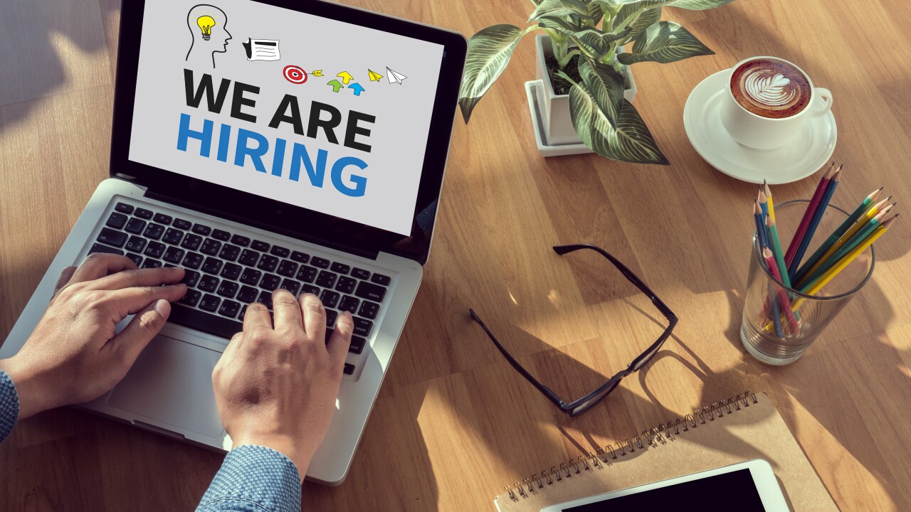 Man typing at computer with a We are hiring screen on his laptop