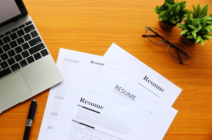 A stack of resumes next to a laptop
