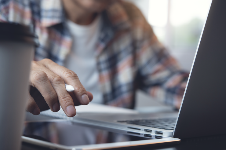 Man typing on a laptop and writing on an iPad.