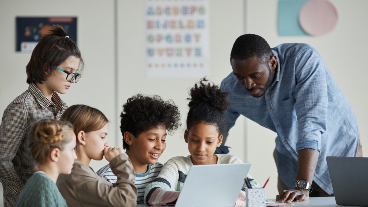 Teacher helps young students as they look at a tablet.