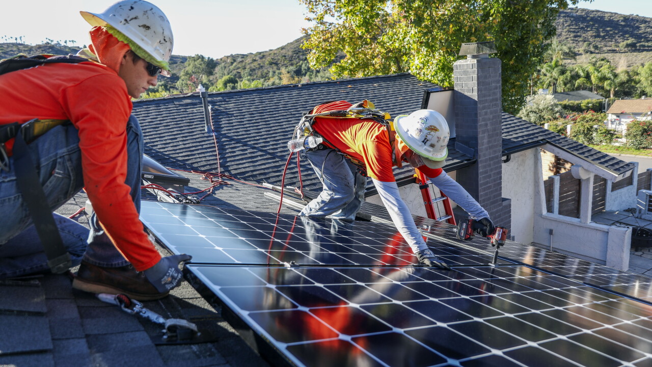 Workers install solar panels on the roof of a home in Poway, California.