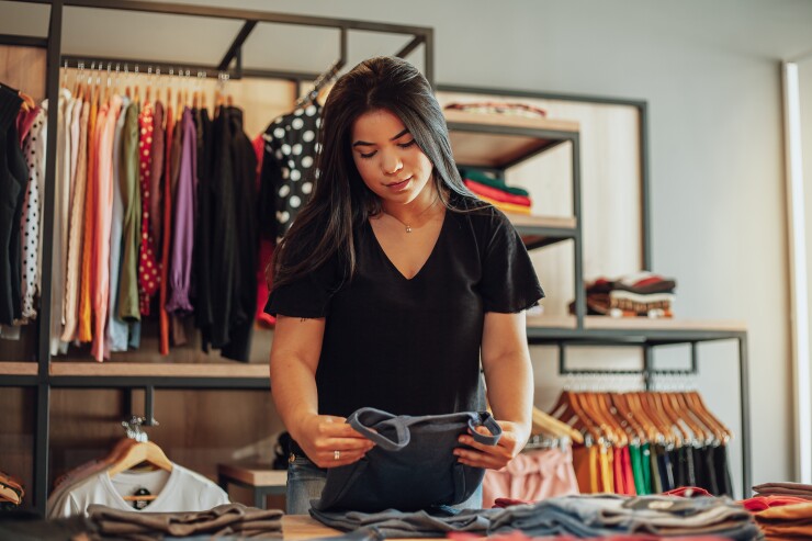 A Latina retail worker is folding a pair of jeans.