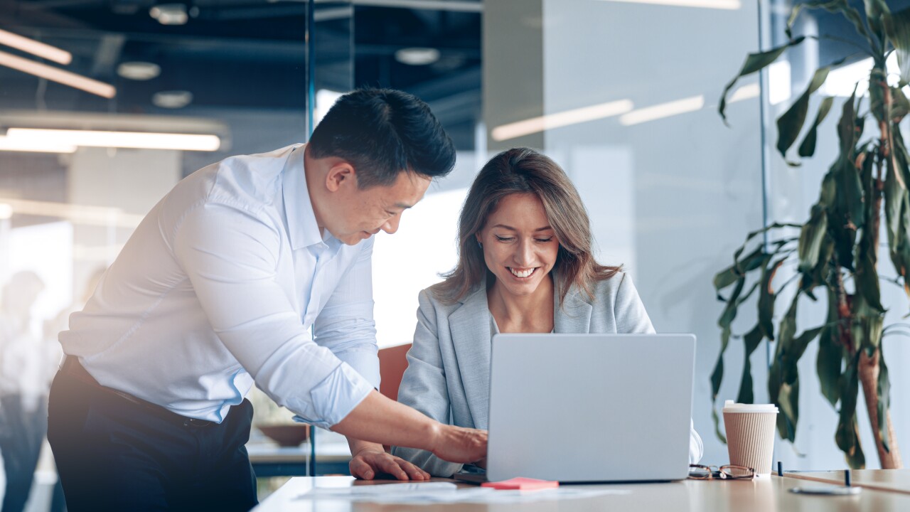 Man and woman in office man helping woman at work woman typing on laptop