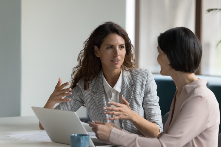Two women talking, sitting at table in office