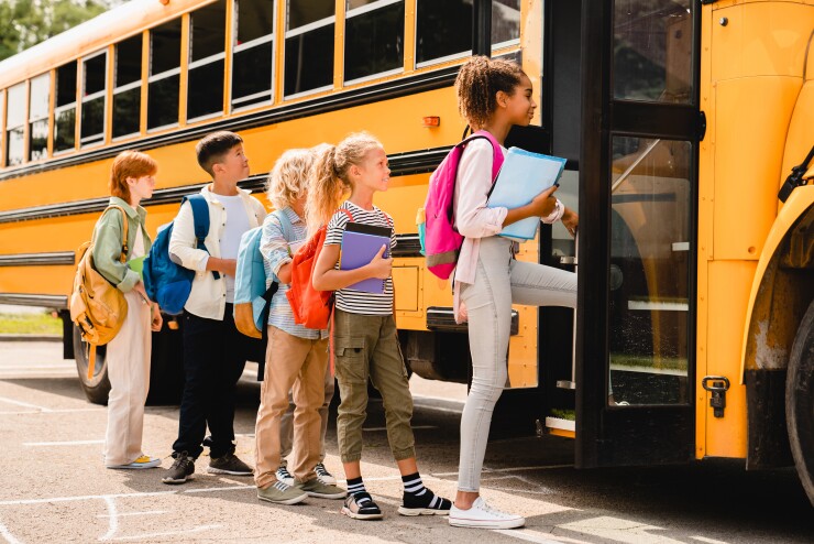 A line of elementary school kids gets on a yellow school bus in the morning.