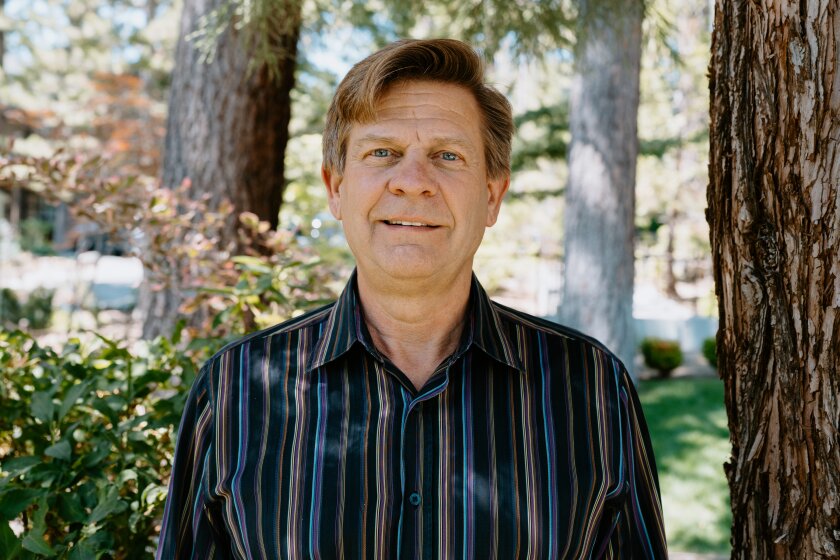 Chris Lewis stands in front of tree trunks.
