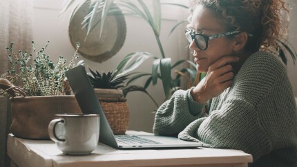 Serene woman work with notebook at home smiling at the display. Serene female use laptop indoor with plants in background. Green colours portrait of people and technology. Lady using computer leisure