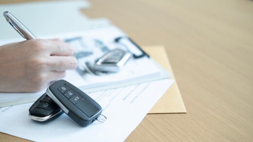 Car remote keys and pen with contract papers showing the process of auto sales deal paperwork and business transaction