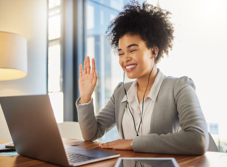 A woman waves at her laptop while on a video call.