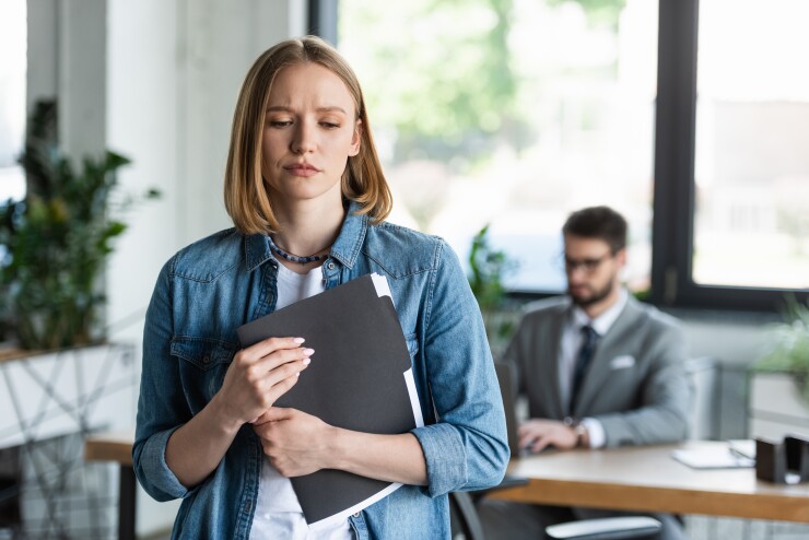 Woman standing in office holding folder, looking upset