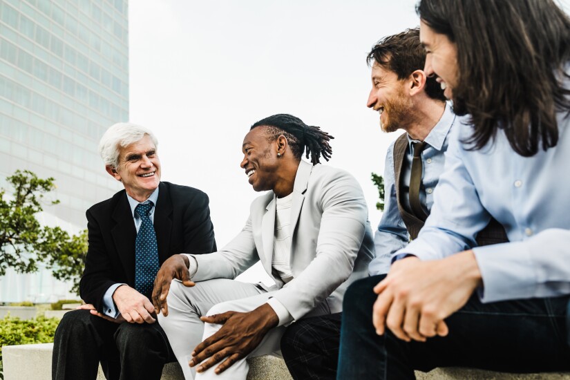 Four men sitting outside office building talking and laughing