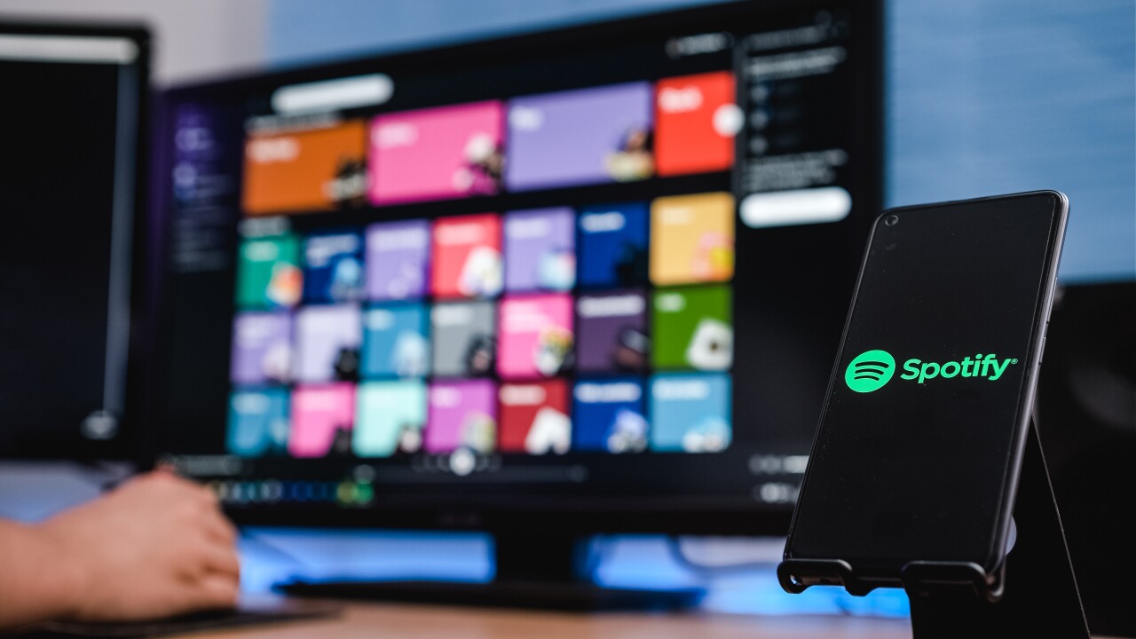 Spotify logo with music playlists in the background on a computer screen.