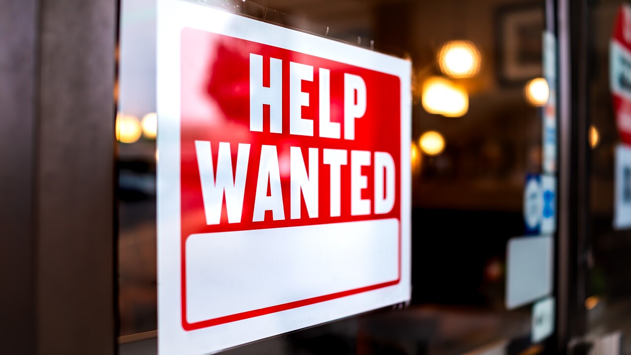 A red and white sign reading "Help wanted" on a glass window pane