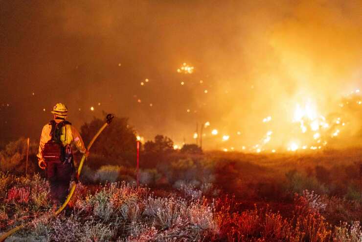 Firefighter holding hose toward raging wildfire
