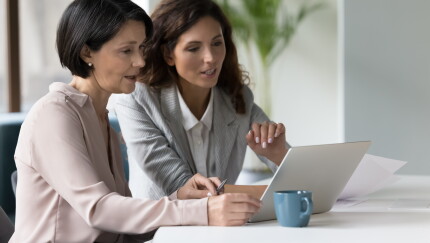 Two businesswomen discuss app or on-line presentation using laptop