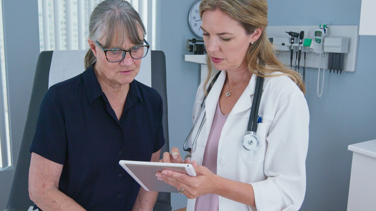 Older female patient sitting on exam table looking at tablet with female doctor