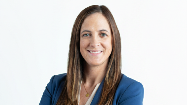 Smiling woman with brown hair wearing a blue jacket and standing against a white background.