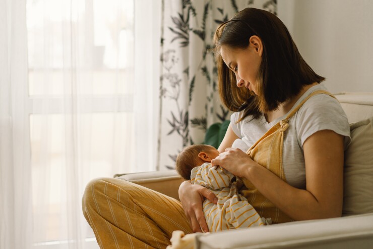 A woman holds her baby to her chest while sitting on her couch.