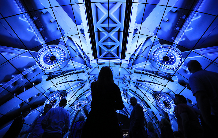 Conference goers walk under a electronic display