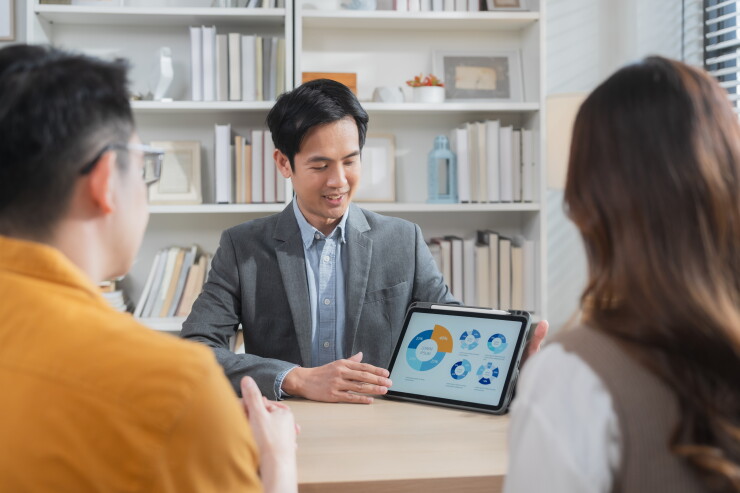 Professional financial advisor presenting investment and savings strategy to couple with tablet analytics, future wealth planning and personal finance consultation concept.