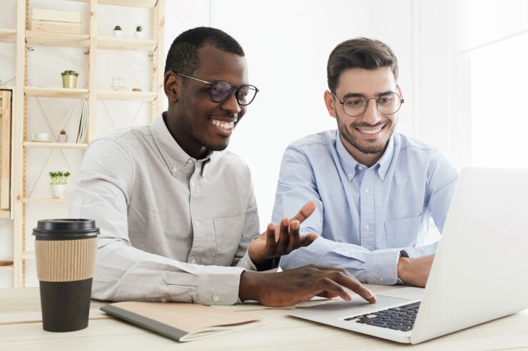 Two male employees working on laptop; smiling