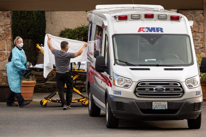 Health care workers transport a patient on a stretcher into an ambulance at Life Care Center of Kirkland, Washington.