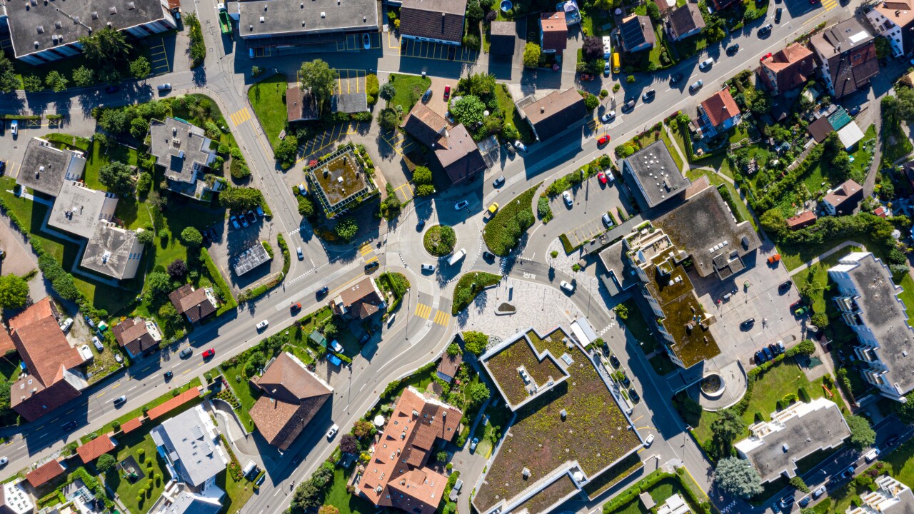 An aerial view of homes, streets with cars driving and other structures.