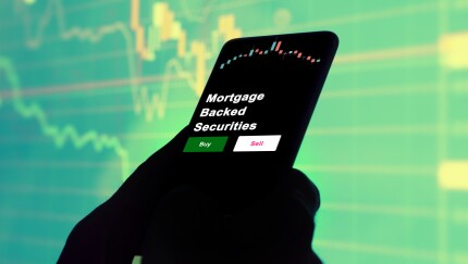 An investor's analyzing the mortgage backed securities etf fund on screen. A phone shows the ETF's prices mortgage backed securities to invest