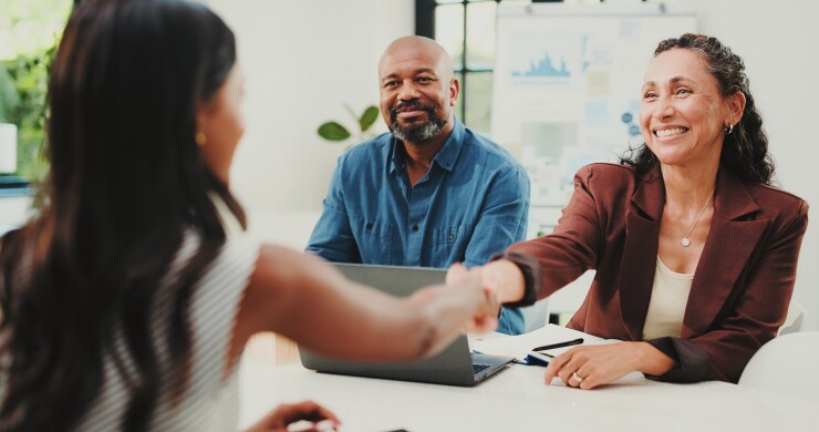 Women shaking hands, man sitting next to woman smiling, job interview
