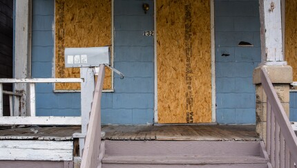 A dilapidated foreclosed home sits boarded up and empty
