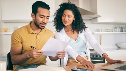 Two people looking at a paper together with a laptop on the counter.